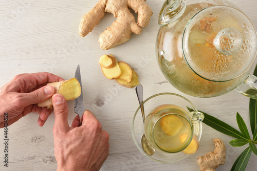 Man preparing ginger infusion on white table with root top