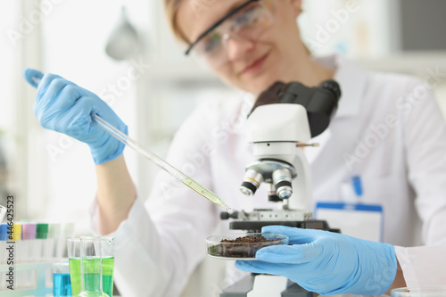 Woman scientist drips liquid oil from pipette into cup of soil