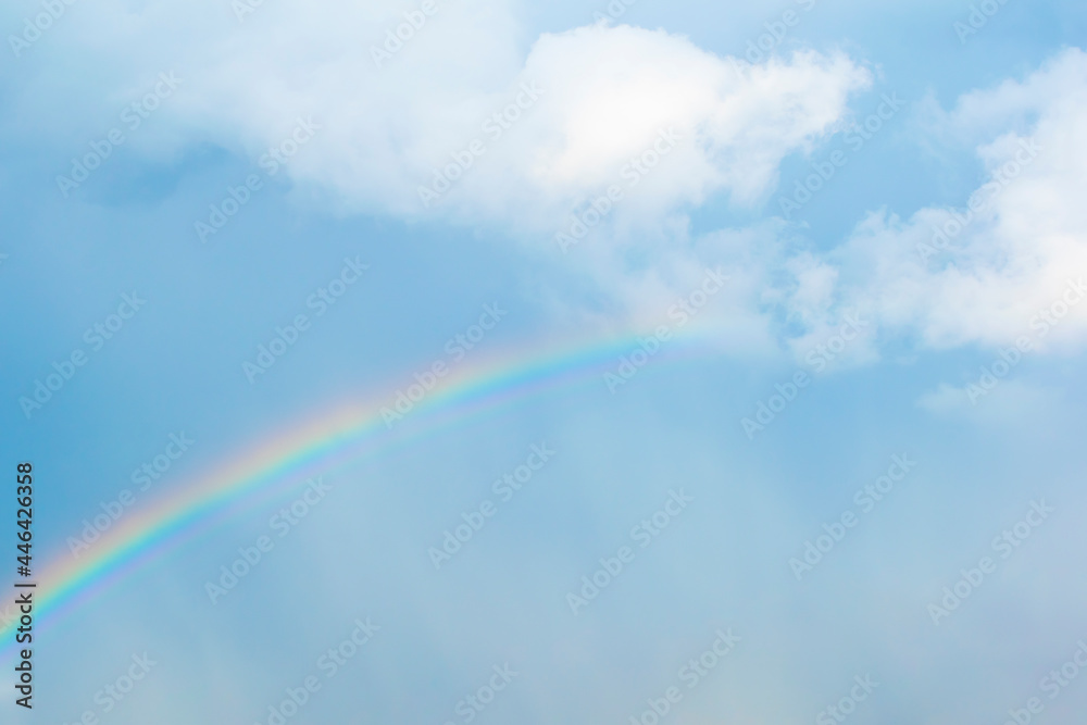 Naklejka premium Rainbow after the storm in the blue cloudy sky, with white cumulus.