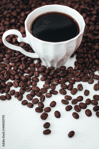 Cup of hot black coffee standing on fresh aromatic roasted coffee beans isolated on white background. Vertical