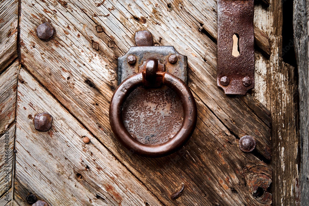 Heavy rusty iron door knocker, ring in front of rectangular iron plate on weathered grained massive old wooden door at the entrance of castle complex Heavy rusty iron door knocker, ring in front of rectangular iron plate on weathered grained massive old wooden door at the entrance of castle complex