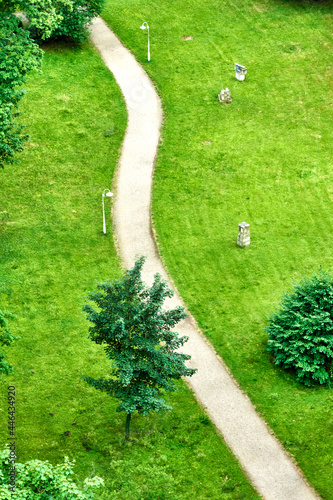 Abstract aerial view of winding footpath running along trees and bushes through manicured lawn area