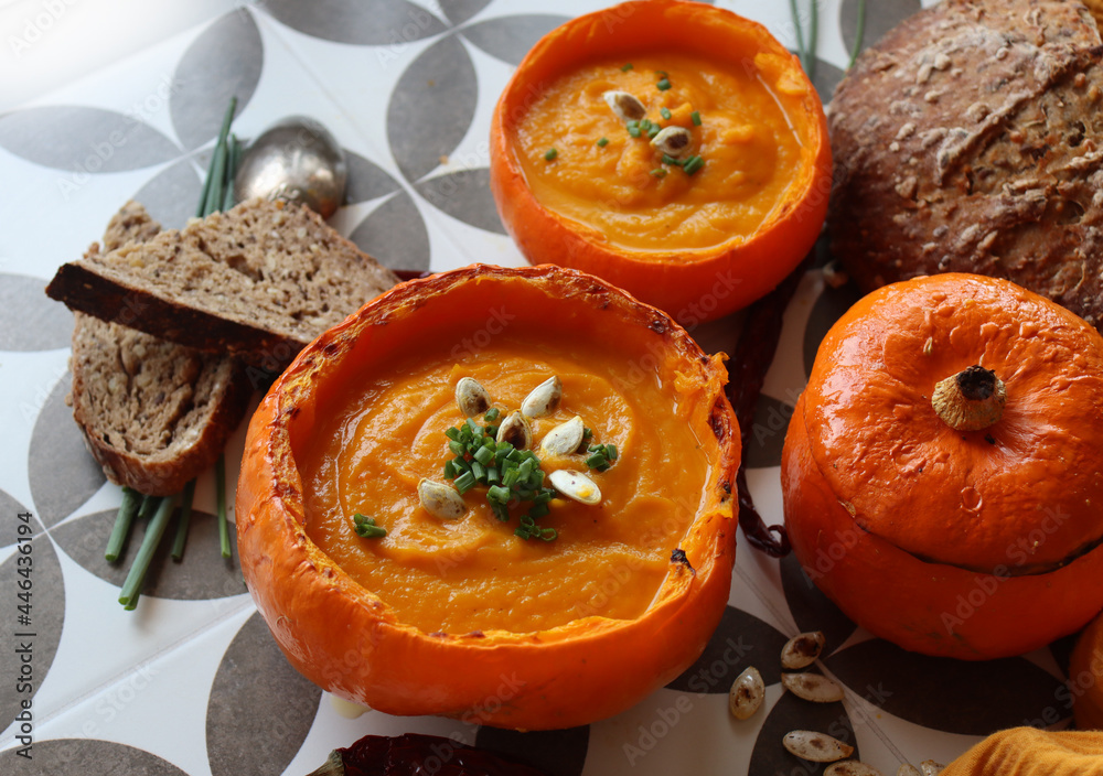 Creamy pumpkin soup and homemade bread on grey tiled table. Soup in a squash top view photo. Thanksgiving menu ideas.  
