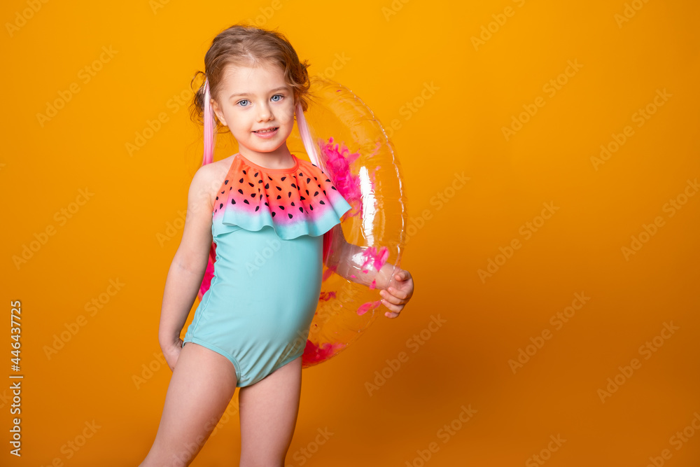 Funny little girl in swimming suit with swimming inflatable ring smiling having fun on yellow background.