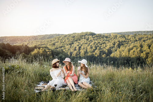 Three stylish happy female friends having fun on outdoor picnic party, eating tasty gourmet french food.