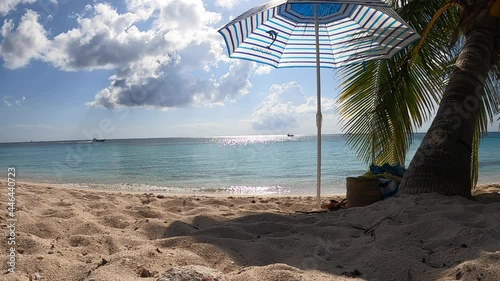 Spiaggia tropicale con un ombrellone vicino ad una palma in riva al mare nell'isola di Cozumel in Messico. Nello sfondo cielo blu e barche in navigazione photo