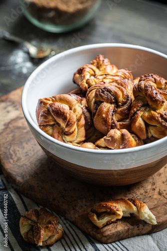 Bowl with freshly baked cinnamon yeast knot buns on dark background .