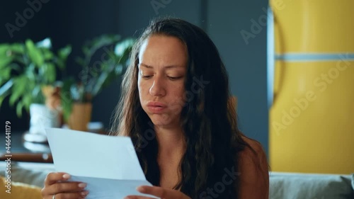 Young woman siting on couch holding documents papers feels. Frustrated girl reads financial loss notice, bank debt bill, failed exam test results or subpoena photo