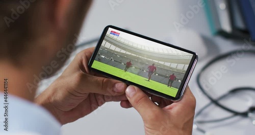 Composite of male doctor watching rugby match on smartphone
