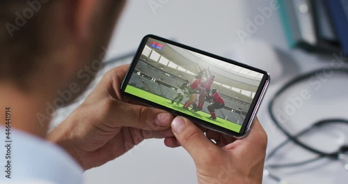Composite of male doctor watching rugby match on smartphone