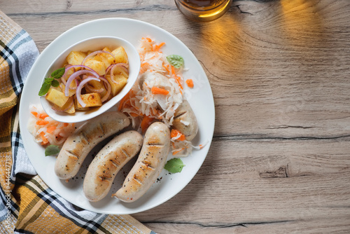 Plate with fried german white sausages, potato salad and sauerkraut, above view on a brown wooden background, horizontal shot with space