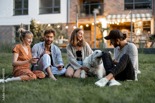 Sticker Young friends having fun playing with a dog and drinking wine, sitting on the gr