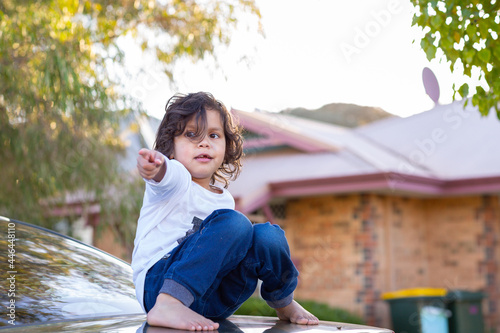 Little kid sitting on car boot pointing photo