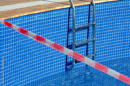 Selective focus on pool with no-entry tape. Red and white tape prohibits entry to swimming pool. Ban on visiting public places during the coronavirus epidemic.