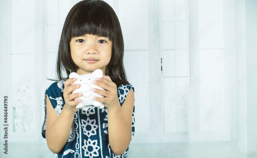 Asian little girl hand holding white piggy bank, learn to saving for the future concept Asian little girl hand holding white piggy bank, learn to saving for the future concept