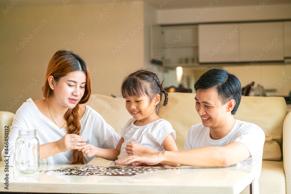 Asian family teach their daughter to saving money and putting coins into glass bank spend a quality time together. Asian family, relationship, happiness and investment concept Asian family teach their daughter to saving money and putting coins into glass bank spend a quality time together. Asian family, relationship, happiness and investment concept
