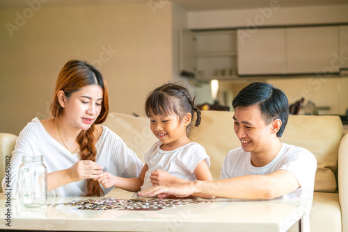 Asian family teach their daughter to saving money and putting coins into glass bank spend a quality time together. Asian family, relationship, happiness and investment concept