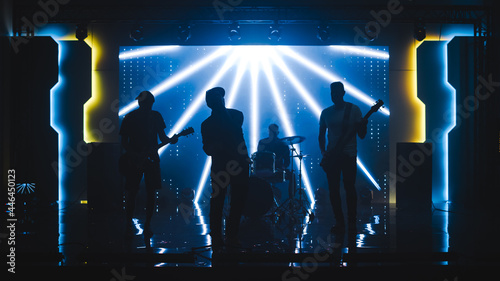 Four Man Rock Band with Lead Singer, Guitarists, Bassist and Drummer Performing at a Concert in a Night Club. Live Music Party in Front of Bright Colorful Strobing Lights on Stage. 