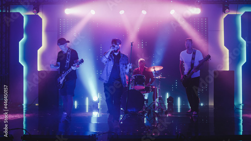 Four Man Rock Band with Lead Singer, Guitarists, Bassist and Drummer Performing at a Concert in a Night Club. Live Music Party in Front of Bright Colorful Strobing Lights on Stage. 