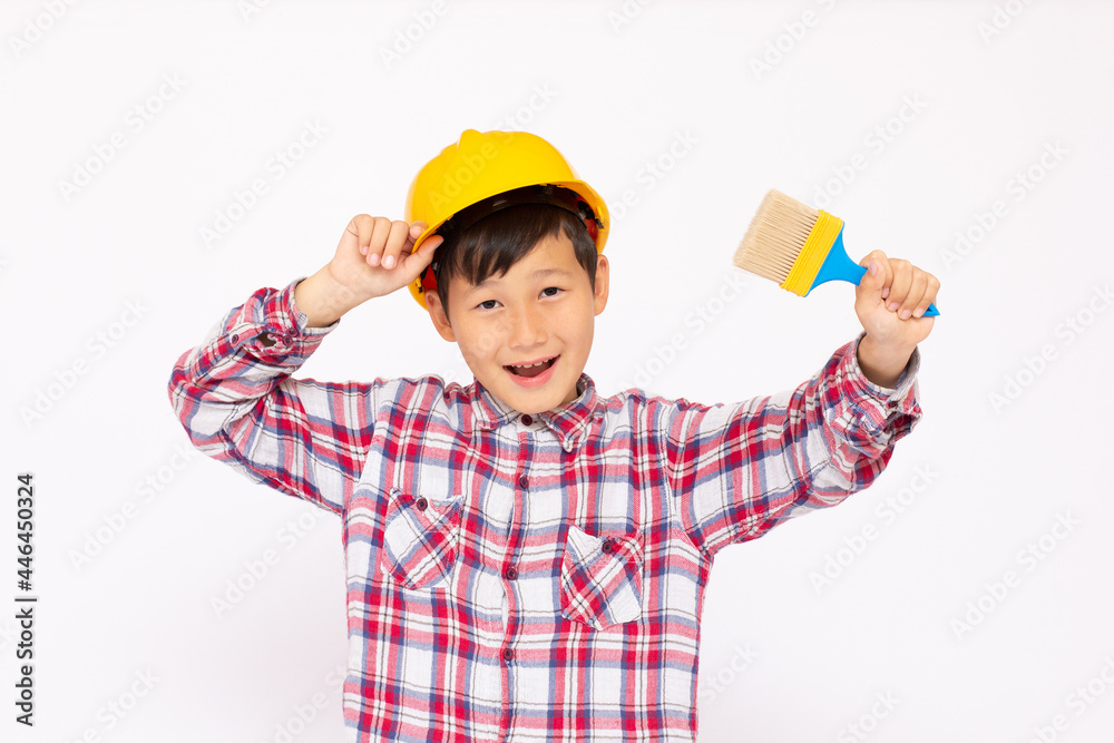 Little kid as a construction worker wearing yellow helmet with a paintbrush in his hand..White background studio picture. Little kid as a construction worker wearing yellow helmet with a paintbrush in his hand..White background studio picture.