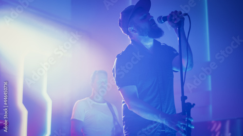 Rock Band Performing at a Concert in a Night Club. Portrait of a Lead Singer Singing into Microphone. Live Music Party in Front of Bright Colorful Strobing Lights on Stage. 