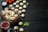 Tasty raw tortellini with flour and basil, on black wooden table background , with copyspace  and space for text