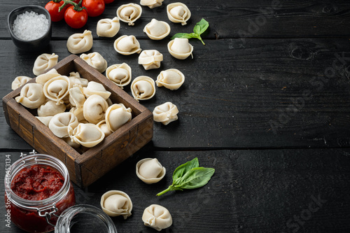 Tasty raw tortellini with flour and basil, on black wooden table background , with copyspace and space for text