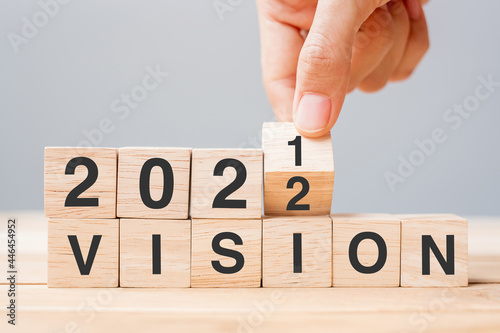 Businessman hand holding wooden cube and flip over block 2021 to 2022 VISION on table background. Resolution, plan, goal, mission, value and New Year holiday concepts