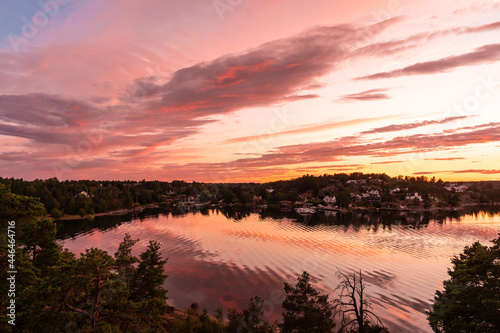 Amazing Beautiful sunset on the Baltic Sea. Bright golden orange pink purple tones of the sunset sky. Rocky Islands of Stockholm archipelago covered with evergreens. Villas on the other coast shore.