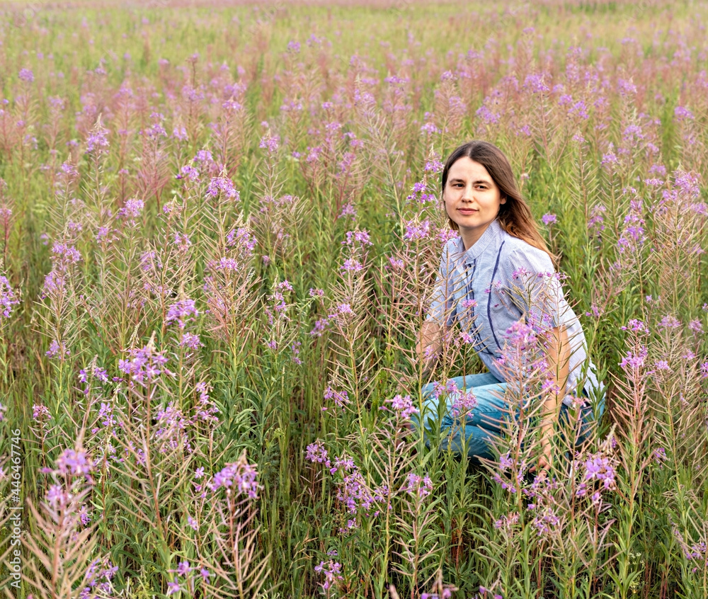 Young beautiful blond woman in purple shirt sitting in the meadow among flowers of fireweed, beauty in nature landscape enjoing the nature Young beautiful blond woman in purple shirt sitting in the meadow among flowers of fireweed, beauty in nature landscape enjoing the nature