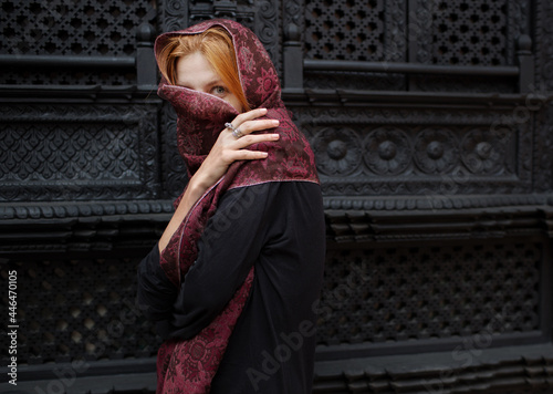 red hair woman in a cashmere scarf stands against the background of the window photo