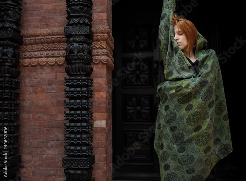 red hair woman in a cashmere scarf stands against the background of the door