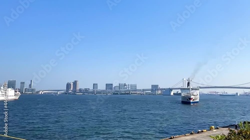 TAKESHIBA, TOKYO, JAPAN - APRIL 2021 : View of Takeshiba port (ferry terminal), Tokyo bay, ship and bridge at Odaiba area. Time lapse tracking shot in sunny day time. photo