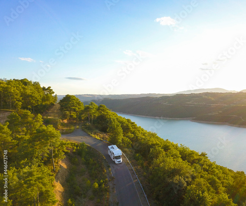 Awesome aerial drone view of an incredible lake road with a van driving it at sunset.