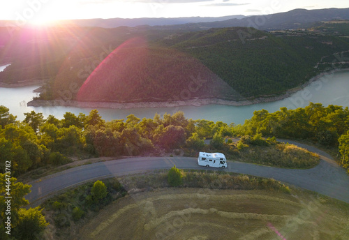 Awesome aerial drone view of an incredible lake road with a van driving it at sunset.