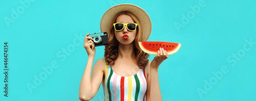 Summer portrait of stylish young woman with retro camera and slice of fresh watermelon wearing a straw hat posing on blue background