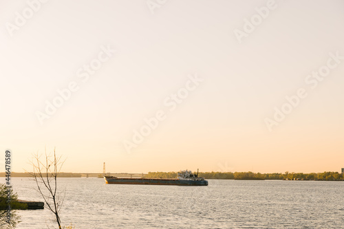 The Bulk carrier is loaded by coal on the anchorage of the port. An empty moored barge is waiting on the sunset to the bulk carrier. Cars goes on the bridge behind the ship. © smishura