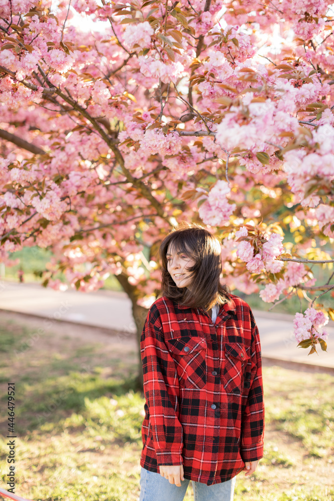 Outdoor portrait of young beautiful Caucasian teen girl smiling and looking into camera, blossom par full of cherry trees on a windy day. 4K footage with sunlight rays Outdoor portrait of young beautiful Caucasian teen girl smiling and looking into camera, blossom par full of cherry trees on a windy day. 4K footage with sunlight rays