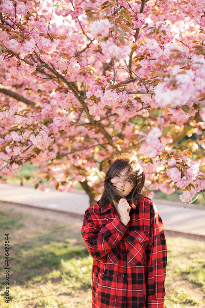 Outdoor portrait of young beautiful Caucasian teen girl smiling and looking into camera, blossom par full of cherry trees on a windy day. 4K footage with sunlight rays Outdoor portrait of young beautiful Caucasian teen girl smiling and looking into camera, blossom par full of cherry trees on a windy day. 4K footage with sunlight rays