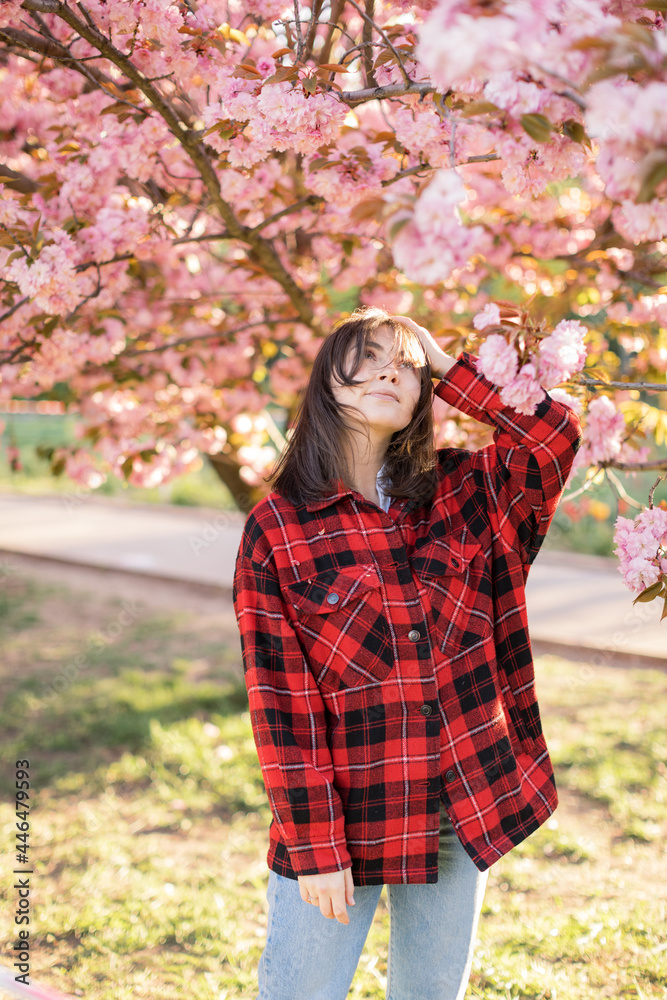 Outdoor portrait of young beautiful Caucasian teen girl smiling and looking into camera, blossom par full of cherry trees on a windy day. 4K footage with sunlight rays Outdoor portrait of young beautiful Caucasian teen girl smiling and looking into camera, blossom par full of cherry trees on a windy day. 4K footage with sunlight rays