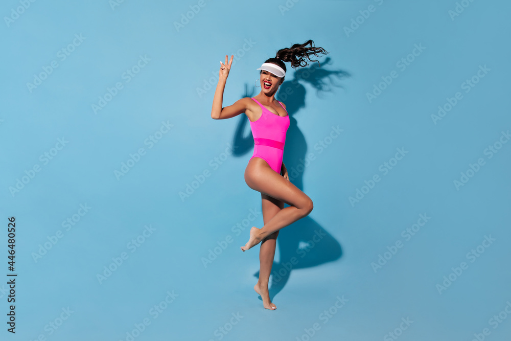 Happy stylish woman with modern hairstyle and bright lips in fashionable pink swimming suit and cap on blue isolated background.. Happy stylish woman with modern hairstyle and bright lips in fashionable pink swimming suit and cap on blue isolated background..