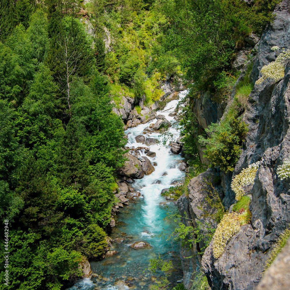 Aerial drone view of a waterfall in a river with turquoise water located in a green natural environment in Pyrenees, Spain.