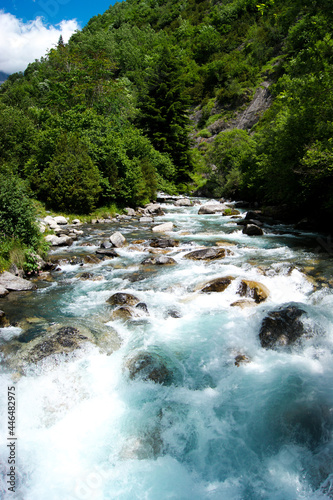 Turquoise water of a river flowing quickly through a green natural landscape in Pyrenees.