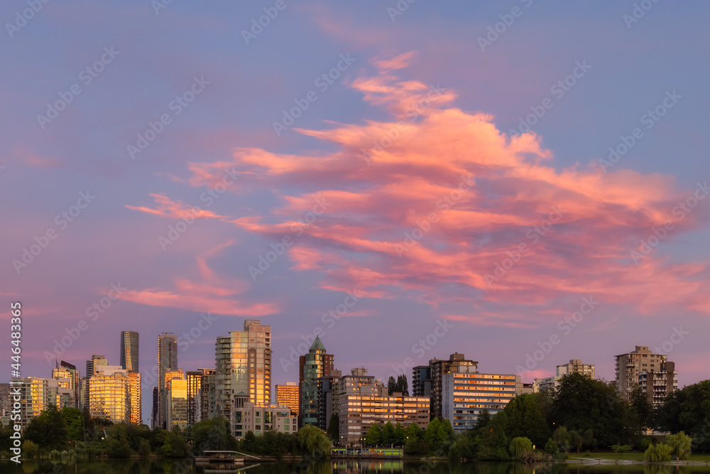 View of Lost Lagoon in famous Stanley Park in a modern city with buildings skyline in background. Colorful Sunset Sky. Downtown Vancouver, British Columbia, Canada.