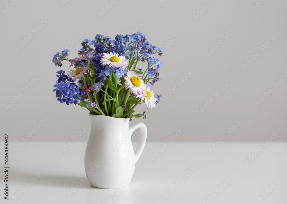 Flowers bouquet in jug on a white table. Daisies and forget-me-nots bouquet. Minimal composition for Valentines day, Mothers day. Copy space.