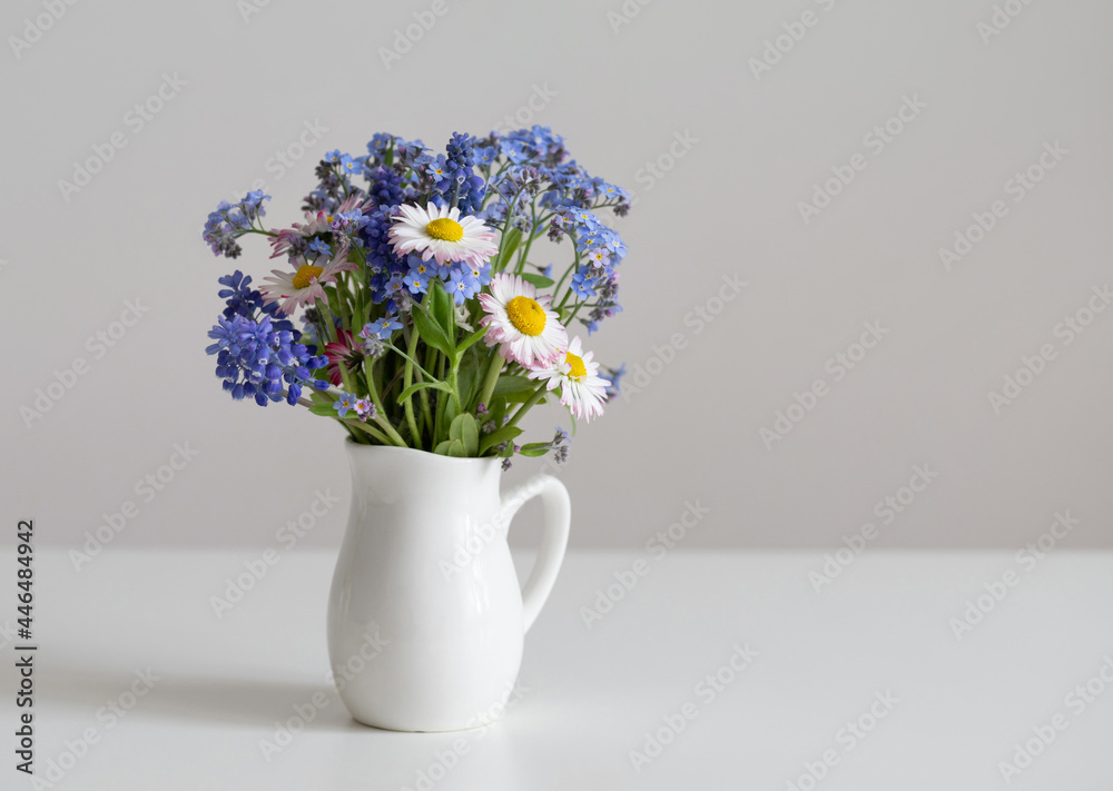 Flowers bouquet in jug on a white table. Daisies and forget-me-nots bouquet. Minimal composition for Valentines day, Mothers day. Copy space. Flowers bouquet in jug on a white table. Daisies and forget-me-nots bouquet. Minimal composition for Valentines day, Mothers day. Copy space.