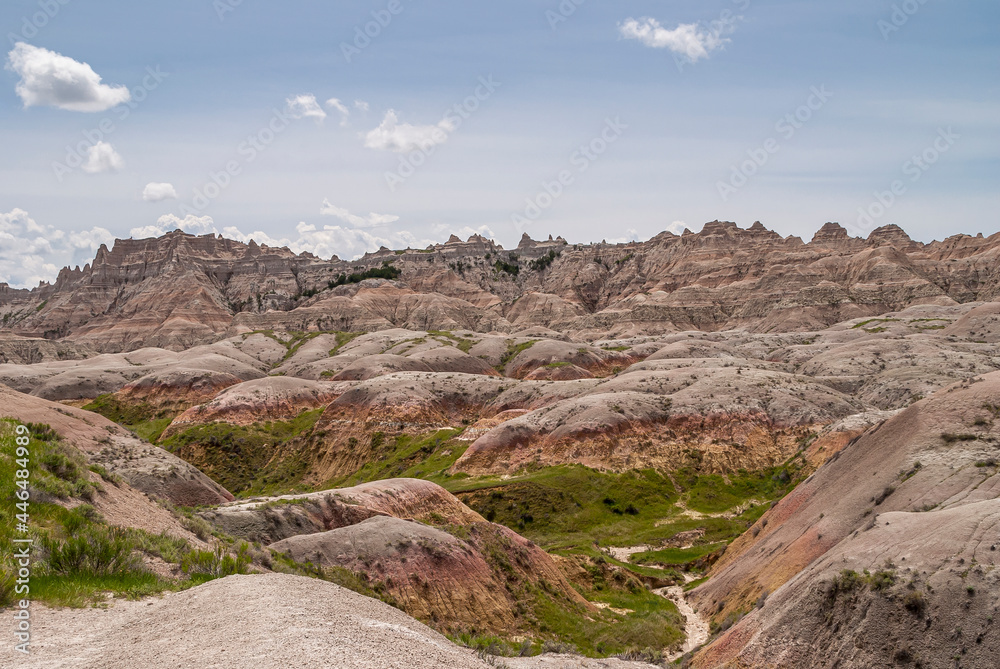 Fototapeta premium Badlands National Park, SD, USA - June 1, 2008: A bad place to loose a calf is this wirwar of geological maroon-gray upcrops with a bid of green in between, a mountain range in back under blue sky.