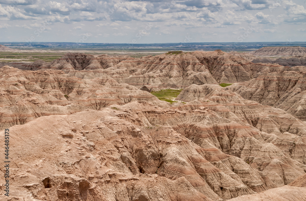 Badlands National Park, SD, USA - June 1, 2008: Wide landscape with mountains cut by red lines over entire range under heavy cloudscape with some green plains on horizon.