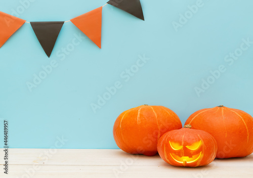 Halloween day. One cute pumpkin with funny face are standing next to colorful flags and to other pumpkins on a blue background. Holiday party. Trick or treat. Greeting card or banner for a store sale