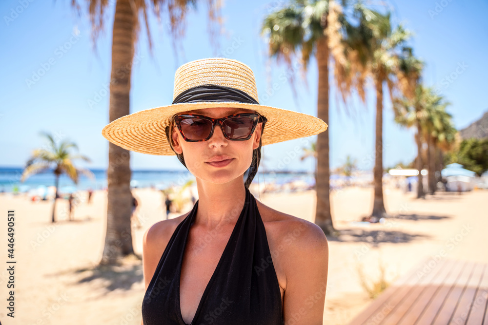 Summer photo of happy woman wearing hat and sunglasses walking on the beach.